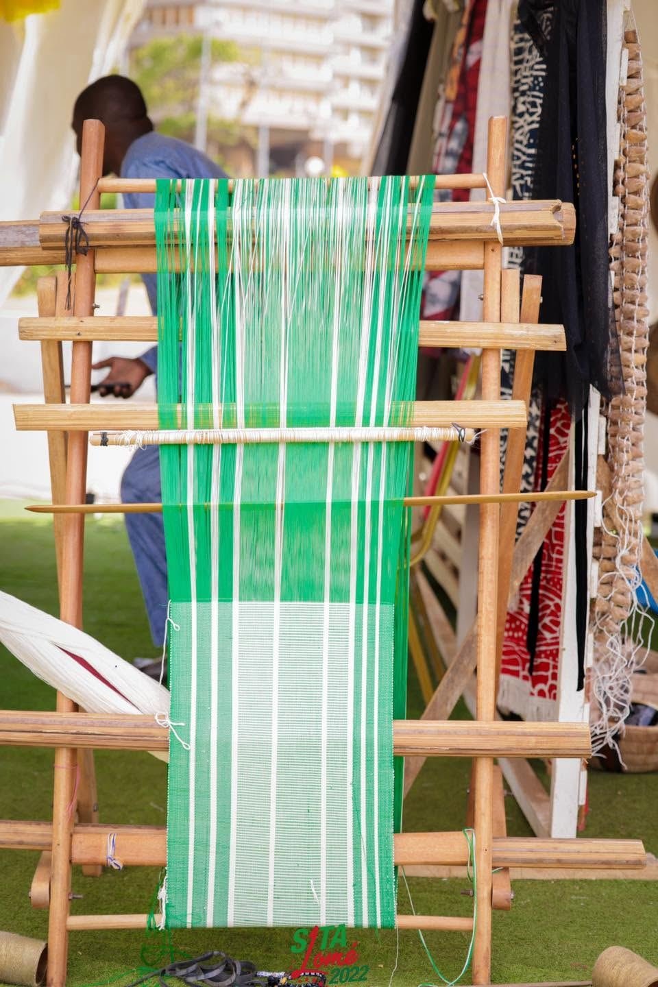 Artisan tissant une bande de pagne traditionnel sur un métier à tisser en bois, SITA Lomé 2022